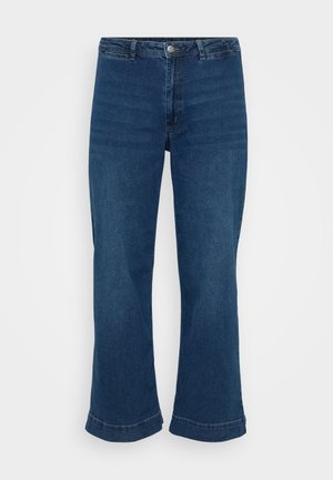 Magas derekú kék farmernadrág egyenes szárakkal és bővülő szegéllyel, denim anyagból készült. Klasszikus öt zsebes kialakítással és fém gombos záródással rendelkezik.