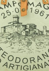 Bolsa de lona con un fondo verde claro, que presenta un dibujo en tinta negra de un edificio y texto en negrita, acentuada con correas de cuero color tostado.