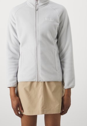 Jasnoszara kurtka polarowa z pełnym zamkiem i dwoma bocznymi kieszeniami, noszona z beżową spódnicą, widziana od szyi do połowy uda na osobie.