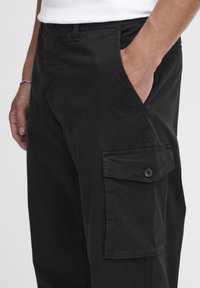 Schwarze Cargo-Hosen aus weichem Stoff, mit seitlichen Taschen, einer knöpfbaren Tasche am Bein und einer schlichten, glatten Textur.