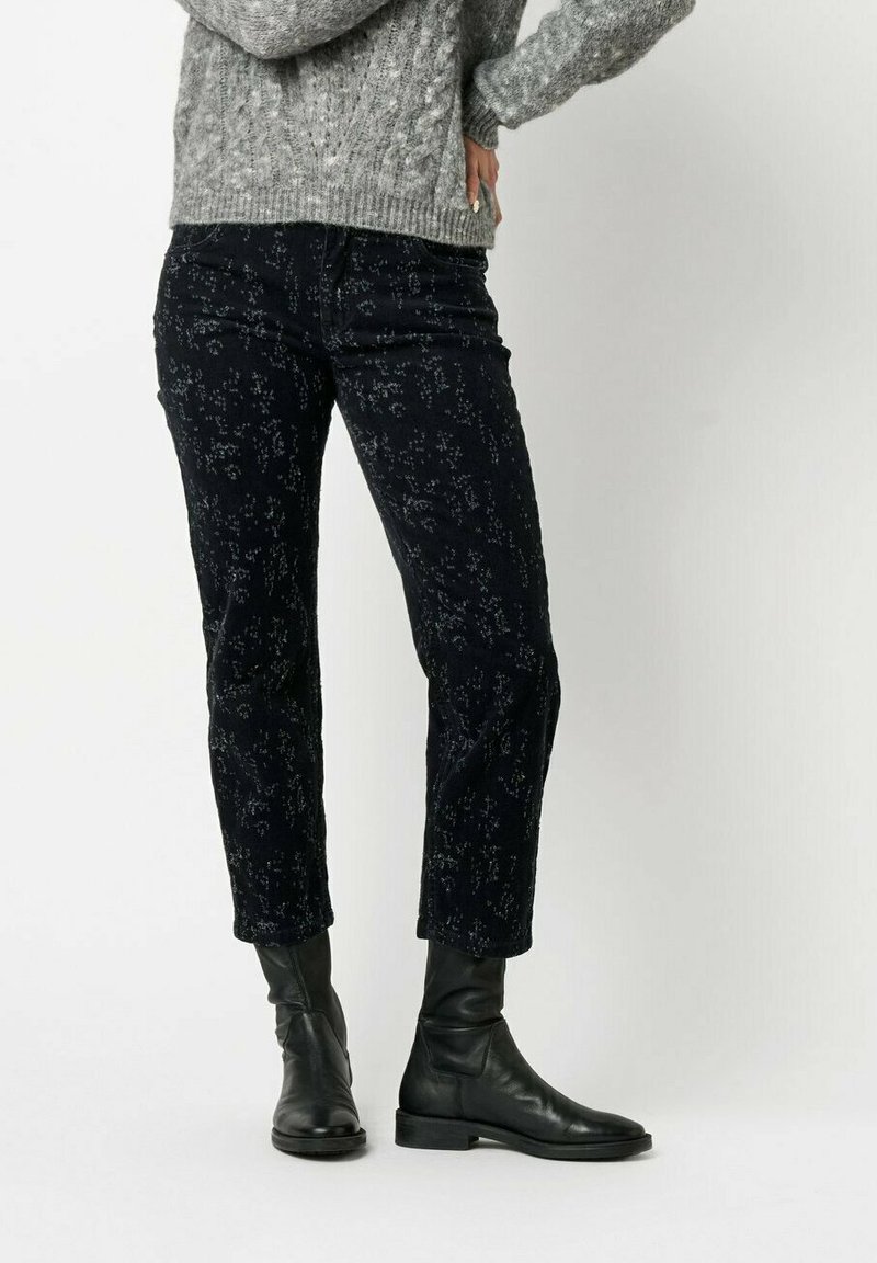 Schwarze gemusterte Hose mit geradem Bein, aus weichem Stoff, mit zartem Blumenmuster und kombiniert mit schwarzen Knöchelstiefeln.