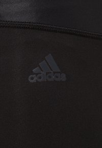 Czarne legginsy sportowe z gładkiego, rozciągliwego materiału. Posiadają subtelne logo Adidas w ciemnoszarym kolorze na dolnej części nogawki. Dopasowany krój.