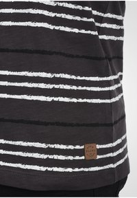 Sorte t-skjorte med horisontale hvite og svarte striper, med en teksturert, vevd etikett nederst som står "Denim Blend Attitude."