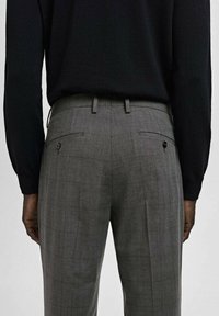 Pantalones a cuadros grises con un corte entallado, que cuentan con dos bolsillos traseros con botones y una textura de tela suave. Acompañados de una camisa negra.