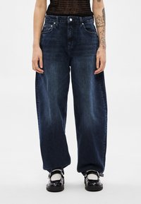 Tmavomodré široké rifle s vysokým pásom, vyrobené z denimu, s tradičným päťvreckovým strihom a jemným vyblednutím na stehnách.