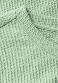 Mintgrön strukturerad tyg med ribbat mönster, har en rundad halsringning och sydda kanter, vilket visar mjukhet och elastisk förmåga.