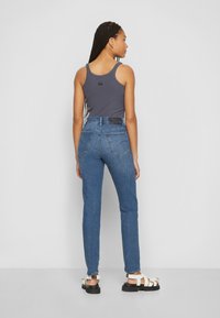 Mørk grå ribbet tanktopp kombinert med blå høy-hukede jeans. Merkbare detaljer inkluderer en svart etikett på livlinjen og hvite stroppesandaler.