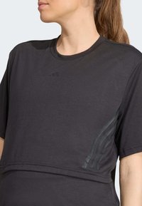 Sort atletisk T-shirt med korte ærmer, rund halsudskæring og diskrete tonale tre-stribe detaljer på siden. Fremstillet af et blødt stof.
