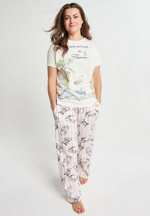 Woman wearing white “Stop and Smell the Flowers” shirt and pink-striped pajama pants with black and white animal prints, standing barefoot.