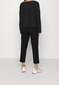 Czarna bluzka z długim rękawem o szerokim dekolcie, zestawiona z czarnymi prostymi spodniami i białymi trampkami z brązowymi akcentami. Gładka tekstura na całej powierzchni.