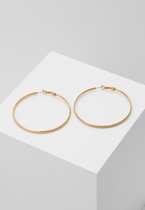 Een paar dunne getextureerde gouden oorringen met een haaksluiting, rustend op een witte schuine ondergrond.