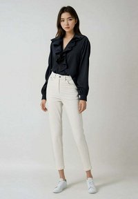 Blouse noire à volants avec des manches longues, associée à un pantalon blanc ajusté et des baskets blanches. Tissu lisse, coupe ajustée, design minimaliste.
