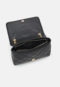 Svart kviltad läderväska med ett lås i guld. Öppen design som avslöjar zip-fack och en slät svart inredning.