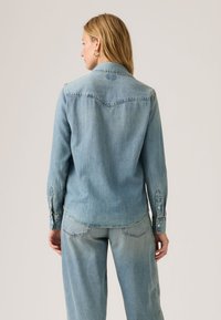 Ανοιχτό γαλάζιο τζιν σακάκι με μυτερό γιακά, μανσέτες με πατώντας κουμπιά και κυρτό τελείωμα. Διαθέτει ραφή στην πλάτη και διακριτικές τσέπες.