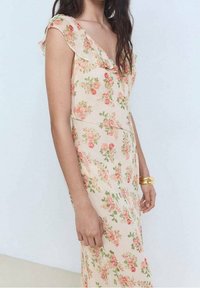 Robe fleurie en tissu pêche pâle, avec un col à volants, des manches courtes et des motifs de roses éparpillés en rose et vert. Texture lisse.