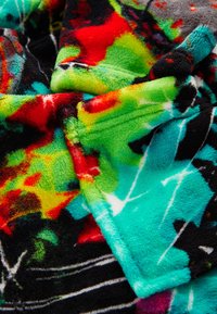 Couverture en polaire colorée affichant des motifs abstraits en rouge, vert, noir et turquoise avec une surface douce et texturée. Lavable en machine.