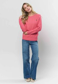 Pink kabelstrik sweater med lange ærmer og ribbede manchetter, parret med flared blå denim jeans og beige slip-on sko.