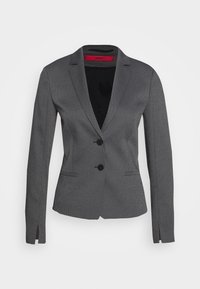 Blazer gris ajusté pour femme en tissu texturé, avec deux boutons noirs, des revers crantés, des poches avant et de petites fentes sur les manches.