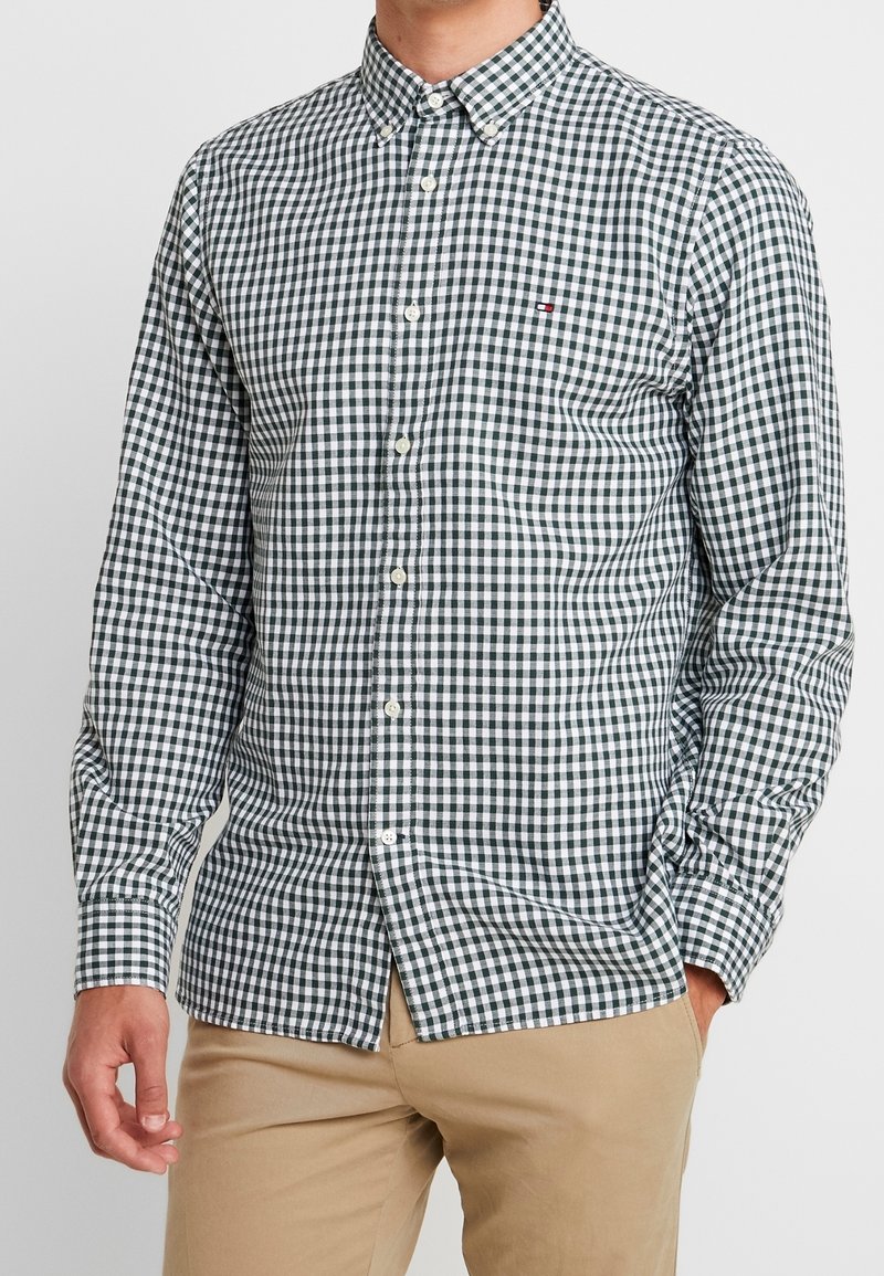Camisa de cuadros verde y blanca, de botones, con cuello, mangas largas y un logo de marca en el pecho, hecha de tela ligera.