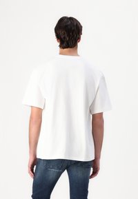 T-shirt en coton blanc à coupe décontractée, à manches courtes et à col rond, associé à un jean en denim bleu.