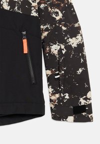 Jas manchetten en onderzijde voorkant met zwart-witte bruine spetterpatroon, ritszak met oranje trekkoord en verstelbare klittenband manchetten.
