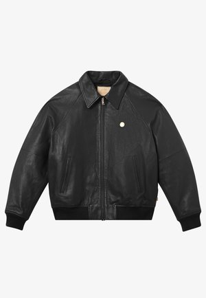 Giacca in pelle nera con zip frontale, polsini e bordo a coste, due tasche laterali e colletto. Presenta un piccolo logo metallico sul petto.