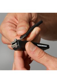 Handen houden en openen een zwarte Tweezerman nagelknipper tegen een effen grijze achtergrond.