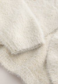 Gros plan d'un tissu doux, blanc et duveteux avec de subtils sequins dorés et des poignets en maille côtelée.