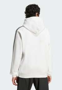 Witte hoodie van een gestructureerde stof, voorzien van een aantrekkoord in de capuchon en zwarte zijstrepen. Het achteraanzicht toont een relaxte pasvorm en geribbelde boorden.