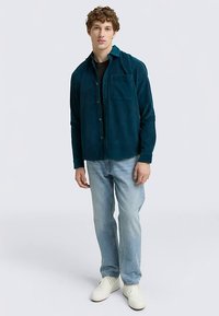 Türkiissinine sametpüksidest särkjope, ees nööpidega, kahe rinnatasku ja lõdva lõikega, kantud hele siniste teksade ja valgete tossudega.