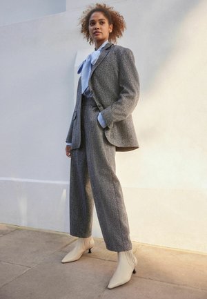 Blazer gri texturat și pantaloni înalți asortați cu buzunare, împerecheați cu o bluză bleu deschis și pantofi cu vârf ascuțit bej.