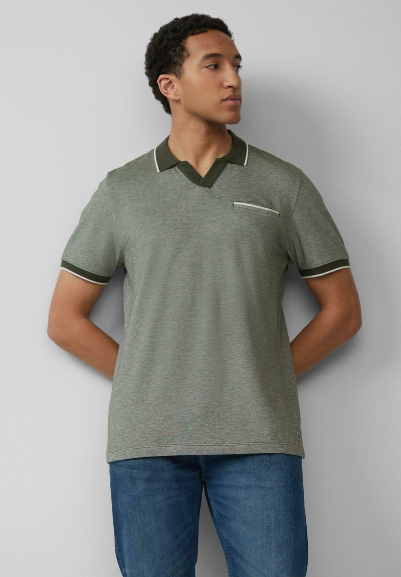 Polo grigio-verde con scollatura a V, colletto verde scuro a contrasto e rifiniture bianche. Presenta una piccola tasca sul petto. Abbinato a jeans blu.