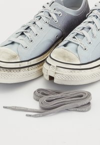Hellblaue Leinenschuhe mit abgenutzten weißen Gummikappen und schwarzem Rand. Mit grauen Schnürsenkeln, auf denen "Chen Wang" gedruckt ist.