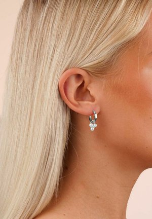 Silberne Creolen mit drei kleinen weißen Perlenakzenten, gestaltet mit einer glatten Oberfläche und einem polierten Look.