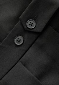 Zbliżenie na czarną tkaninę z dwiema czarnymi plastikowymi guzikami przyszytymi na nakładających się warstwach.