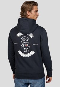 Sudadera de marina hecha de una mezcla de algodón. Presenta un gráfico en la parte espalda de una muñeca con ojos de botón y boca bordada, acentuada con texto blanco y un corazón.
