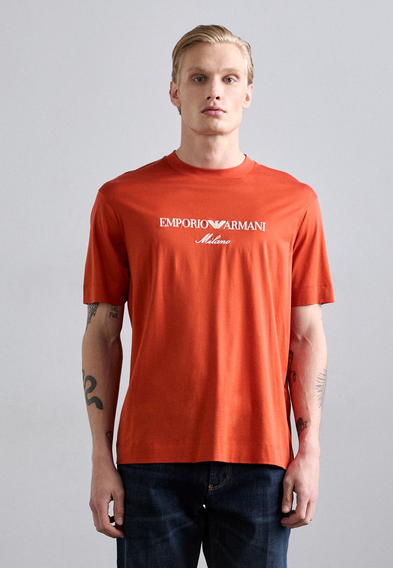 T-shirt en coton rouge à manches courtes arborant le logo Emporio Armani en blanc et un détail de Milan. Design simple avec col rond, ourlet droit et coupe décontractée.