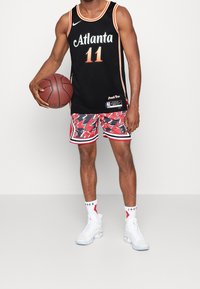 Camiseta de baloncesto negra con "Atlanta" y el número 11, combinada con unos pantalones cortos rojos con estampado, zapatillas blancas y calcetines blancos con acentos rojos.