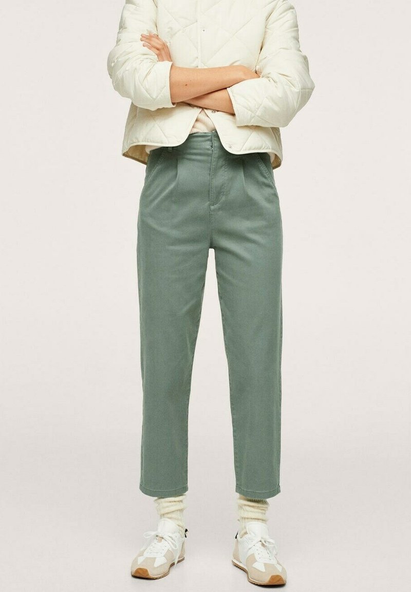 Pantaloni di cotone verdi con vita alta, gamba dritta e pieghe frontali. Abbinati a sneaker bianche e calzini color crema.