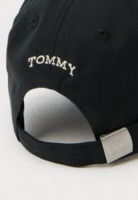 Fekete baseball sapka, fehér hímzett "TOMMY" felirattal a hátoldalon, állítható fém csattal és texturált anyagfelülettel.