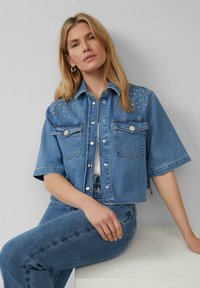 Geknipte denimjack met korte mouwen, lichtblauwe wassing, met versieringen op de schouders en twee voorzakken.