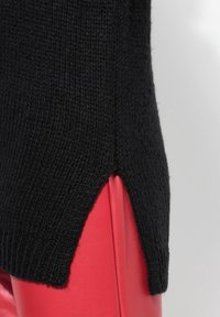 Schwarzer Strickpullover mit einer strukturierten Oberfläche, seitlichen Schlitzen und einer lockeren Passform, kombiniert mit lebhaft roten Lederhosen.