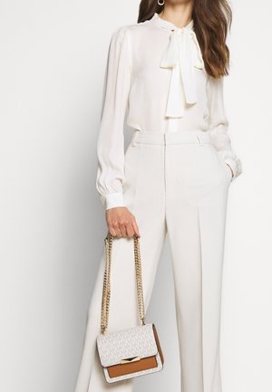 Blouse blanche à manches longues avec un col à nouer, associée à un pantalon crème taille haute à jambes larges. Tenant un sac à main bicolore à motif avec une bandoulière chaîne.