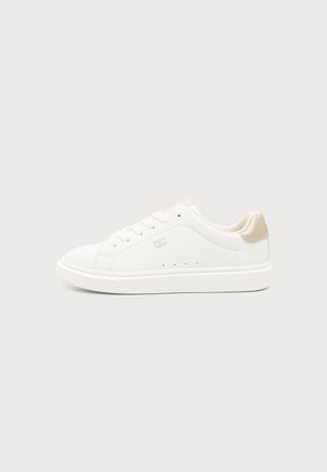 Λευκό χαμηλό sneaker με μπεζ τακούνι, σχέδιο με κορδόνια, μικρό λογότυπο στο πλάι και επίπεδη καουτσούκ σόλα σε απλό ανοιχτό φόντο.