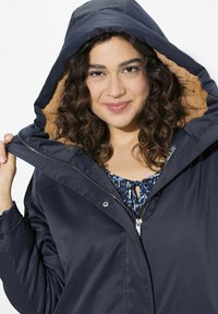 Marinblå vattenavvisande jacka med en plyschfodrad huva och dragkedja, med ett blommönstrat inre lager och justerbara snören.
