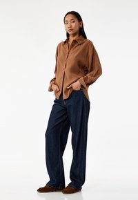 Bruine overhemd, relaxte pasvorm, lange mouwen, gecombineerd met losse donkere spijkerbroek en bruine schoenen. Eenvoudig ontwerp, gladde textuur.