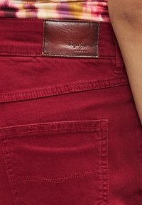 Røde denimjeans med en brun læderlap præget med "Pepe Jeans", subtile syningsdetaljer og standard lommedesign.