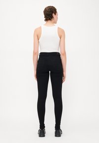 Fekete, magas derekú leggings, rugalmas anyagból, hátsó zsebekkel és slim fit fazonnal. A modellen fehér trikó és fekete cipő található.