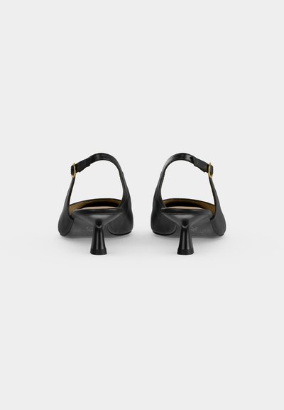 Paire d'escarpins noirs slingback avec fines brides à la cheville et boucles, vues de dos sur un fond uni clair.