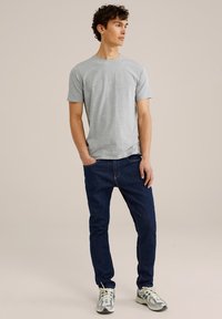 Camiseta gris de manga corta combinada con jeans de color azul oscuro, mostrando un diseño sencillo. El calzado presenta acentos en gris, verde y blanco.